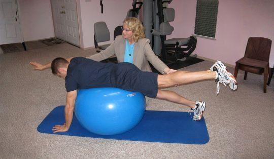 therapist helping a man lying on a ball to exercise back